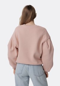 Sudadera de gran tamaño en color rosa pálido con mangas abullonadas, cuello acanalado y textura suave. Combinada con jeans de mezclilla azul claro.