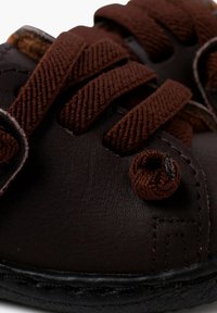 Braune Leder-Kinderschuhe mit strukturierten Oberflächen, ausgestattet mit braunen Schnürsenkeln und runden Schnürlöchern. Schwarze Gummisohle und Nähdetails.