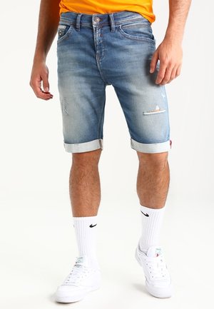 Shorts en denim bleu clair avec ourlets retroussés, présentant des détails usés et une coupe régulière, associés à des chaussettes blanches Nike et des baskets.