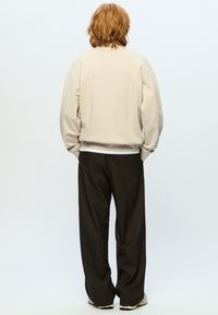 Beige sweatshirt met verlaagde schouders, gecombineerd met losse donkere broek. Minimalistisch ontwerp, gestructureerde stof en neutrale kleurenpalet.