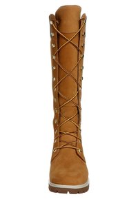 Bota alta de ante beige con cordones, ojales metálicos, cordones marrones y una suela de goma resistente. Acabado liso y diseño aerodinámico.