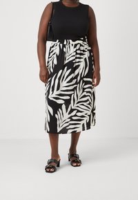 Haut sans manches noir associé à une jupe fluide longueur genoux ornée d'un motif de feuilles de palmier blanches sur fond noir. Sandales noires à talons.