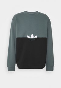 Zeleno-černá mikina s kulatým výstřihem. Na hrudi je bílý vyšívaný logo. Měkká látka, volný střih a dlouhé rukávy.