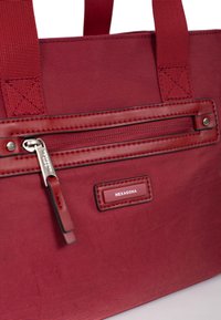 Borsa a spalla rossa in tessuto con tasca anteriore con zip, manici in nylon e un'etichetta con la scritta "HEXAGONA". Texture liscia con dettagli cuciti.
