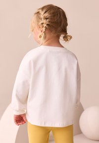 Sweat-shirt en coton blanc à épaules tombantes, poignets côtelés et design simple au dos, associé à un legging jaune.