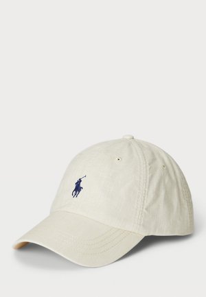 Világos bézs színű baseball sapka, amely szövetből készült, hímzett sötétkék logóval az elején, ívelt napsütés elleni peremmel és szellőző nyílásokkal.