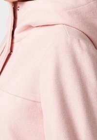 Chaqueta con capucha rosa hecha de una tela suave, que presenta una textura lisa y un brillo sutil, con un primer plano de los detalles del hombro y de la capucha.