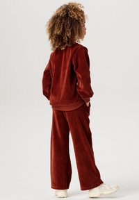 Bränd orange fleece träningsdräkt med en avslappnad passform, som har en rundhals, långa ärmar och byxor med vida ben, som kombineras med ljusa sneakers.