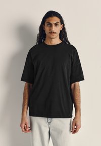 Černé bavlněné tričko s krátkým rukávem, kulatým výstřihem a volným střihem. Nosené s džínovými kalhotami ve světlém praní.