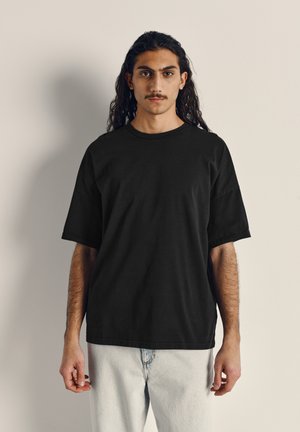 Black cotton t-shirt with short sleeves, a round neckline, and a relaxed fit. Worn with light wash denim jeans.