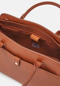 Sac à main synthétique marron avec doubles poignées, fermeture éclair, et une étiquette intérieure de marque ; présente une texture lisse et des détails de couture subtils.