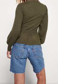 Top a maniche lunghe a palloncino in maglia a coste color verde oliva, abbinato a pantaloni shorts in denim blu con orli sfilacciati e tasche posteriori.