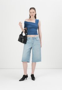 Plavi top na jedno rame s zavijenom tkaninom, svijetloplave traperice culottes i crna torba s izazvanom ručkom. Crne čizme s potpeticama.