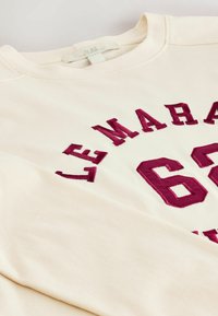 Hanorac bej cu text oversized burgund "LEMAR" și „62” brodat în față. Material moale, guler rotund și mâneci lungi.
