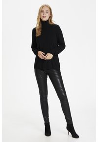 Melnas turtlenecks ar garām piedurknēm, pārī ar melnām mākslīgās ādas legingām un melniem augstpapēžu potīšu zābakiem; visā virsmā gluda tekstūra.
