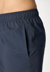 Bermudas atléticas azul-marinho feitas de tecido leve, com um cós elástico e bolsos laterais, apresentando uma textura suave e um design minimalista.