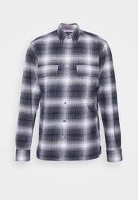 Camisa de franela a cuadros en azul marino y blanco, de manga larga, diseño abotonado con dos bolsillos en el pecho y pequeño detalle de logo cerca del dobladillo.
