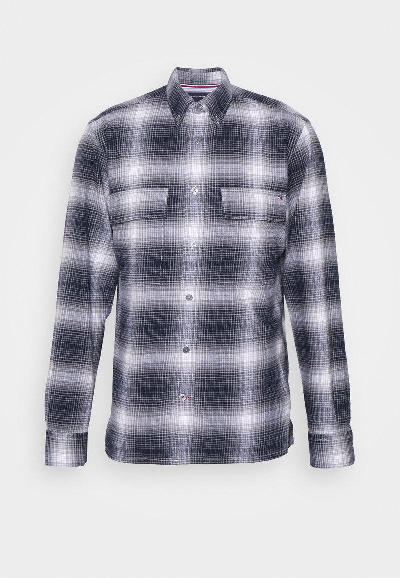 Camisa de franela a cuadros en azul marino y blanco, de manga larga, diseño abotonado con dos bolsillos en el pecho y pequeño detalle de logo cerca del dobladillo.