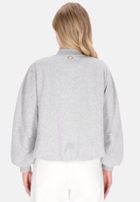 Jasnoszara bluza o luźnym kroju, z zaokrąglonym kołnierzem i bufiastymi rękawami. Z tyłu przy dekolcie znajduje się mały złoty akcent.