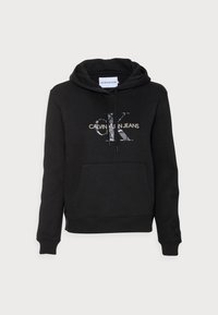 Sudadera con capucha negra que presenta un bolsillo frontal y el logo de "Calvin Klein Jeans" en una mezcla de texturas, diseñada para el uso casual.