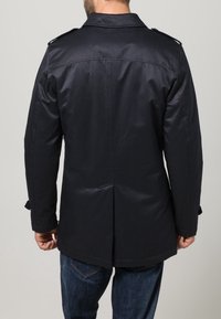 Marinblå kappa med slät textur, designad med axelklaffar och ventilerad rygg, med rak skärning och två fickor.