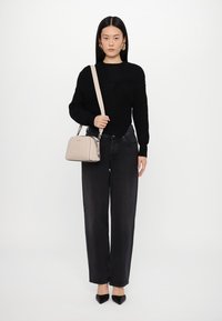 Black textured sweater paired with high-waisted black jeans, a light beige handbag, and black pointed-toe heels. Model in neutral background.