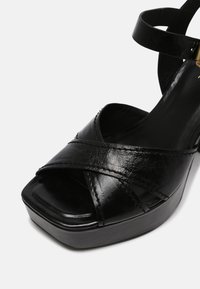Sandale plate-forme en cuir noir avec des brides croisées et une bride de cheville avec une boucle dorée.
