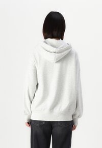 Harmaa huppari pehmeällä pinnalla, jossa on nyörikiinnitys hupussa ja laskeutuvat olkaompeleet, yhdistettynä tummiin farkkuihin. Varustettu ribatulla hihansuut ja helmalla.