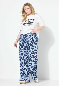 Vit t-shirt med djärv svart text, ihopparad med ljusblå byxor med marinblå leopardmönster och en avslappnad, lös passform. Vita sneakers.
