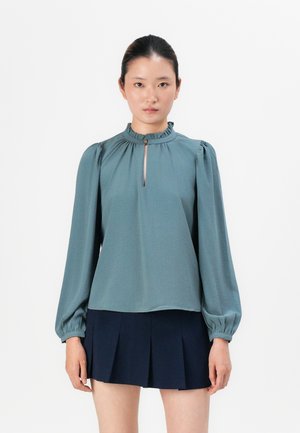 Teal blouse with a ruffled collar, long puff sleeves, and a keyhole opening at the front. Paired with a navy pleated skirt.