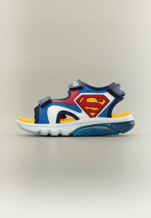 Blauwe, rode en gele kindersandaal met verstelbare bandjes en een rood Superman-logo aan de zijkant.
