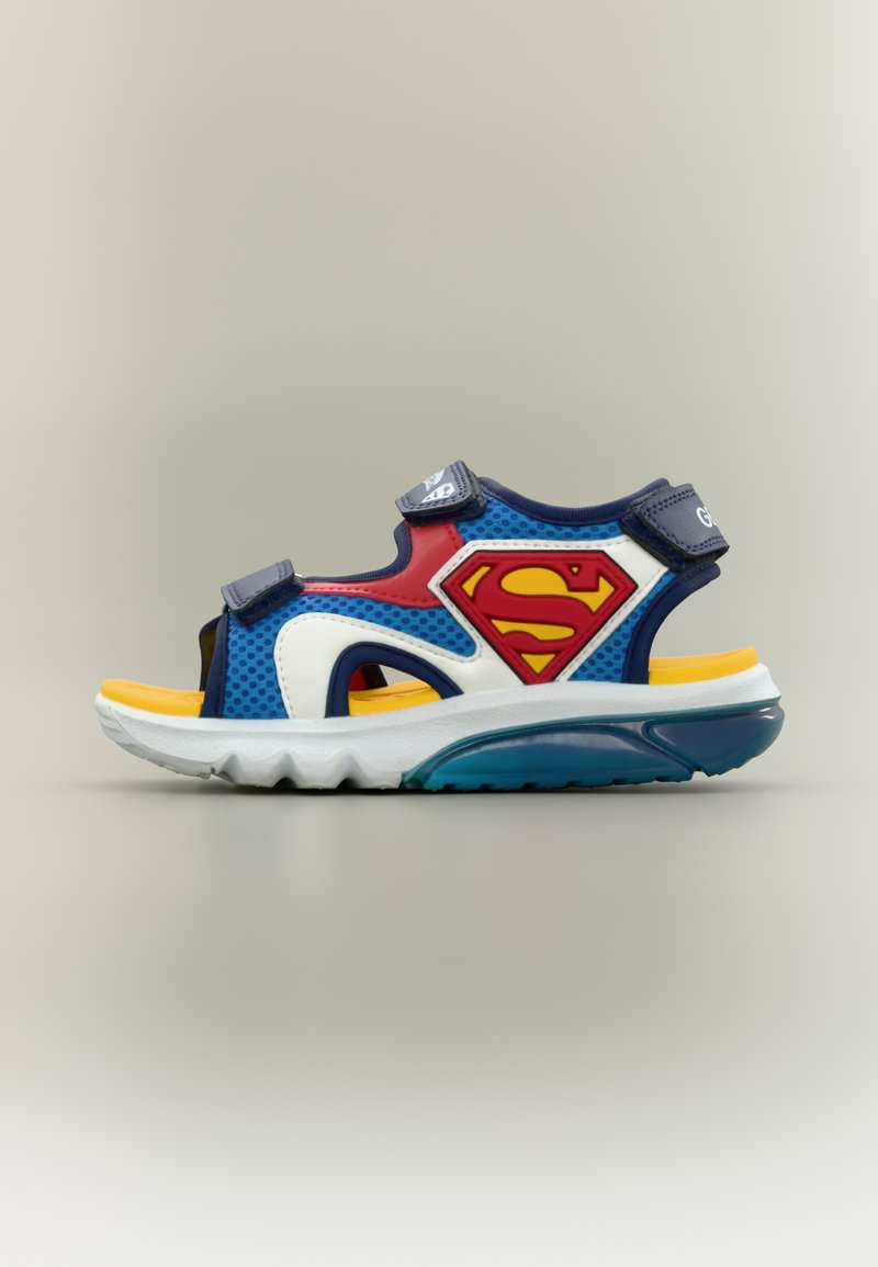 Παιδικό σανδάλι σε μπλε, κόκκινο και κίτρινο με ρυθμιζόμενους ιμάντες και κόκκινο λογότυπο Superman στο πλευρό.