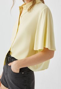 Blouse jaune à manches courtes avec un col boutonné, coupe décontractée et tissu lisse, assortie à un short en denim noir taille haute.