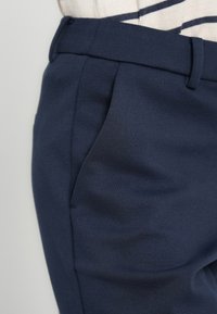 Στενά σαλπάκια σε ναυτικό μπλε με ομαλή, υφή υφάσματος, διαθέτουν πλαϊνές τσέπες και καθαρή μέση.