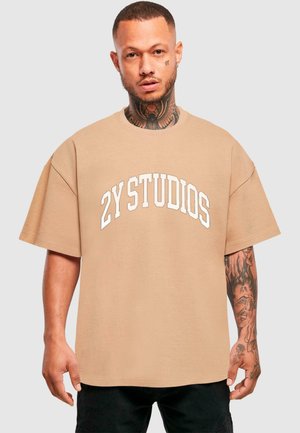 Beige oversized t-shirt med korte ærmer og rund halsudskæring. Har hvid "2Y STUDIOS" tekst på brystet. Blødt bomuldsstof.