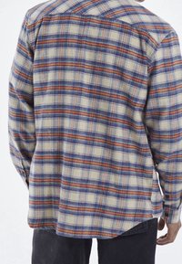 Geruite shirt in beige, blauw en oranje, met lange mouwen, een kraag en een rechte onderkant. Het materiaal lijkt textuur te hebben en geweven te zijn.