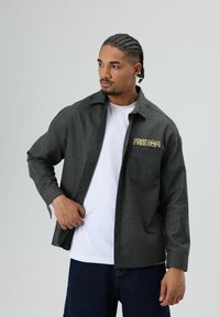 Heren overhemd met ruitpatroon in donkergrijs en groen, met een ontspannen pasvorm, knoopsluiting en een gele "FREEDOM" borduring op de borst.