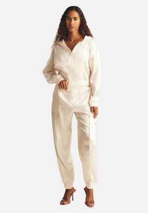 Completo sportivo bianco in satin con giacca con cappuccio e zip e pantaloni con vita elastica, caratterizzati da polsini, linee morbide e una vestibilità rilassata.