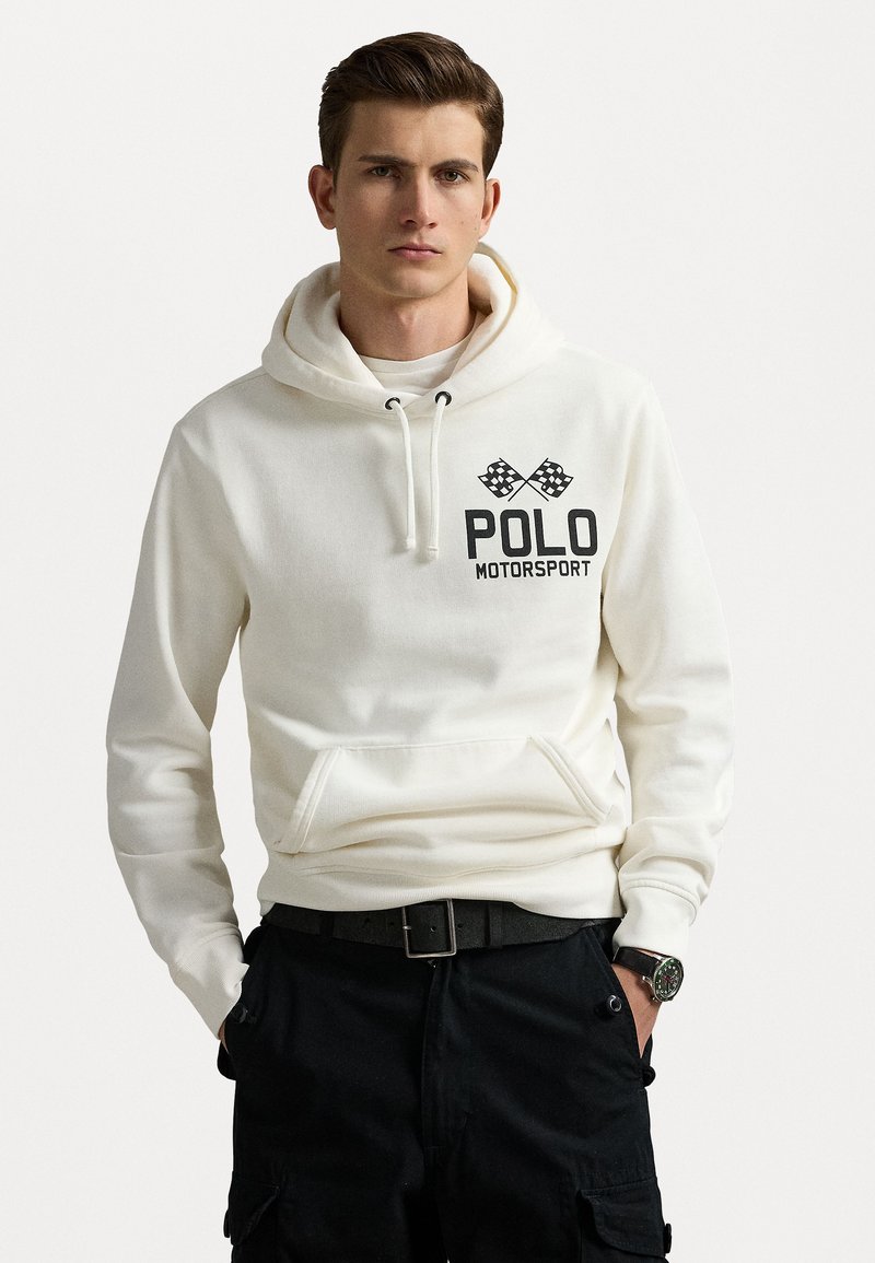 Balta kokvilnas kapuce ar priekšējo kabatu, auklu kapuci un melnu "POLO MOTORSPORT" logo ar šaha karogiem. Nēsāta ar tumšiem biksēm.