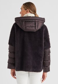 Daunenjacke in Dunkelbraun mit einem strukturierten Strickrücken, ausgestattet mit einer gequilteten Kapuze und enganliegenden Ärmeln mit genähten Akzenten.