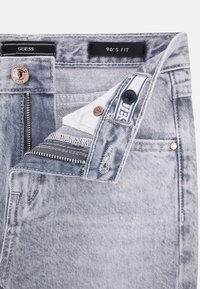 Light grey denim jeans with a 90's fit. Features a button closure, zipper fly, and visible stitching details. Brand tag displayed inside.