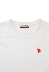 Bílý bavlněný tričko s kulatým výstřihem a malým červeným vyšitým logem na levé hrudi. Na štítku je uvedeno U.S. Polo Assn.