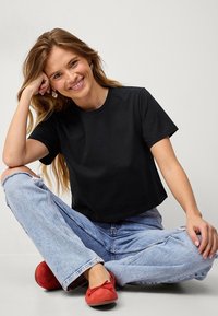Zwarte cropped t-shirt van zachte katoen, korte mouwen, ronde halslijn, gecombineerd met lichtblauwe hoge taille jeans en rode flats.