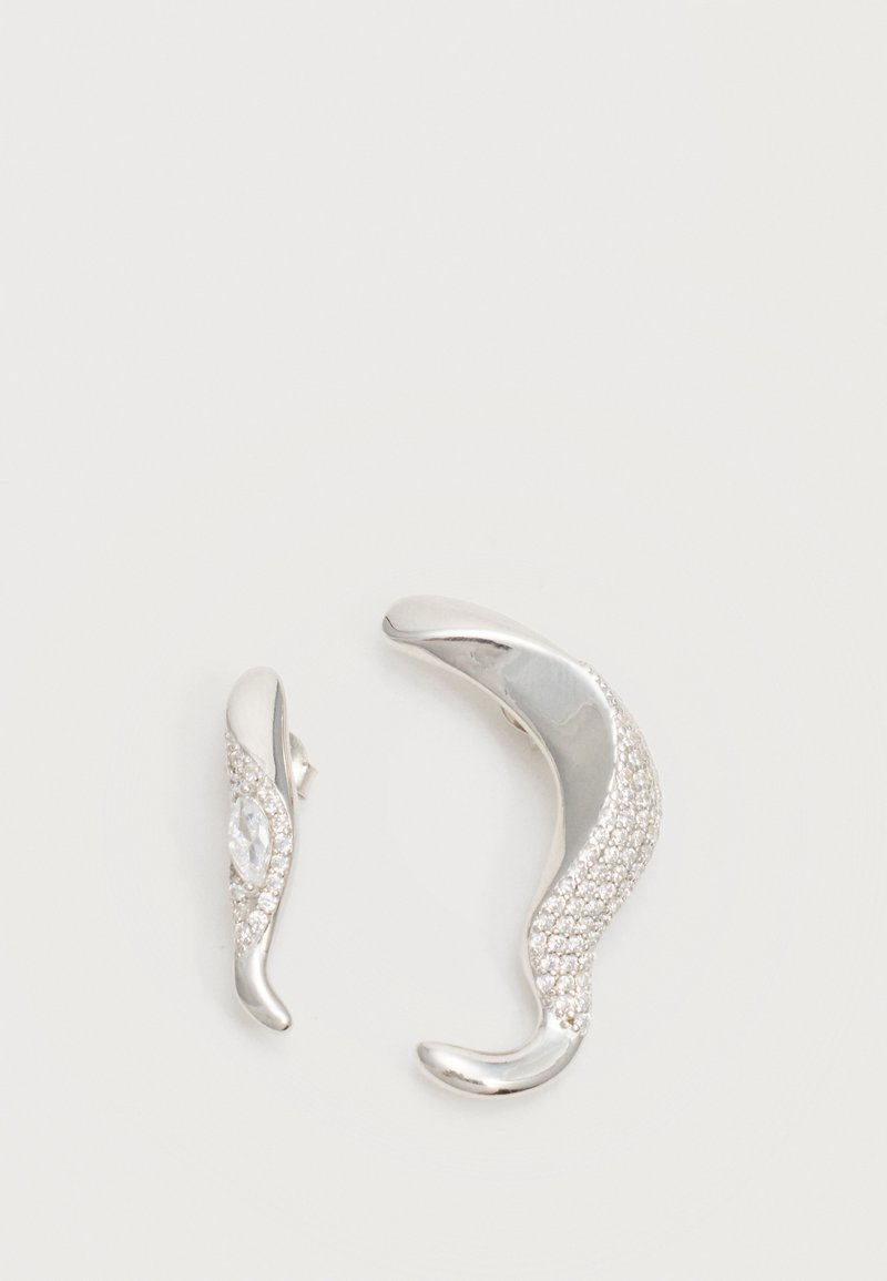 Deux boucles d'oreilles argentées courbées, l'une plus grande que l'autre, toutes deux ornées de petits cristaux scintillants le long d'un bord.