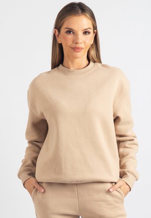 Beżowa bluza z miękkiej tkaniny, z okrągłym dekoltem, ściągaczami na mankietach i luźnym krojem, dobrze komponująca się z pasującymi spodniami.