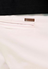 Gros plan sur la poche arrière d’un pantalon rose clair avec une étiquette en cuir marron de la marque Jack & Jones à côté de l’ourlet d’une chemise noire.