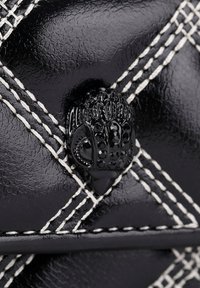 Borsa nera in pelle trapuntata con cuciture bianche e una fibbia decorativa nera che assomiglia a una mano. Texture liscia con finitura lucida.