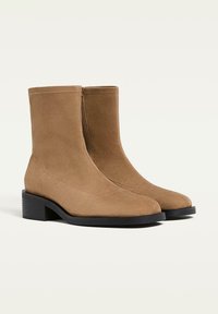 Stivali alla caviglia in suede marrone con tacco a blocco, texture liscia, punta arrotondata e zip laterale per un facile indossamento.