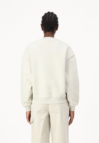 Hellgrau oversized Sweatshirt mit rundem Halsauschnitt und gerippten Bündchen, von hinten betrachtet; glattes, strukturiertes Material.