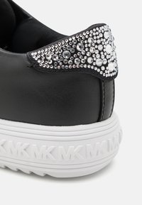 Talons de baskets noirs avec des strass clairs regroupés sur le haut du dos et une semelle blanche embossée du logo MK répétitif.